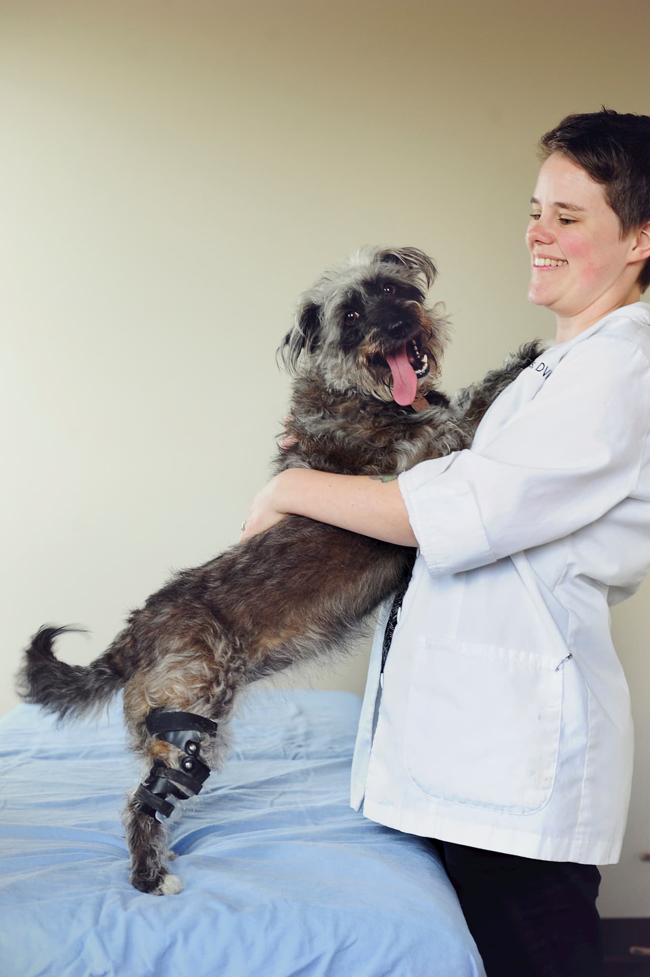 Veterinarian hugging a smiling dog after fitting with a knee brace for torn ACL