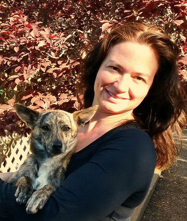 Dr. Annette Richmond holding a dog outdoors with red leafy plants in the background